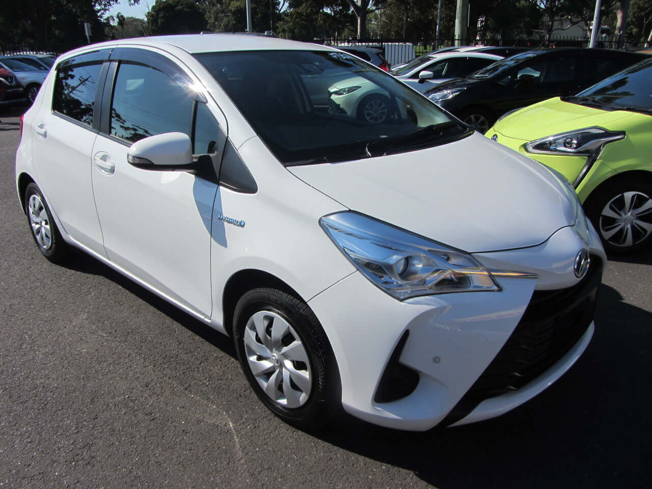 2018 Toyota Vitz 1.5L Hybrid, white compact car, parked with other vehicles in background, showing design features.