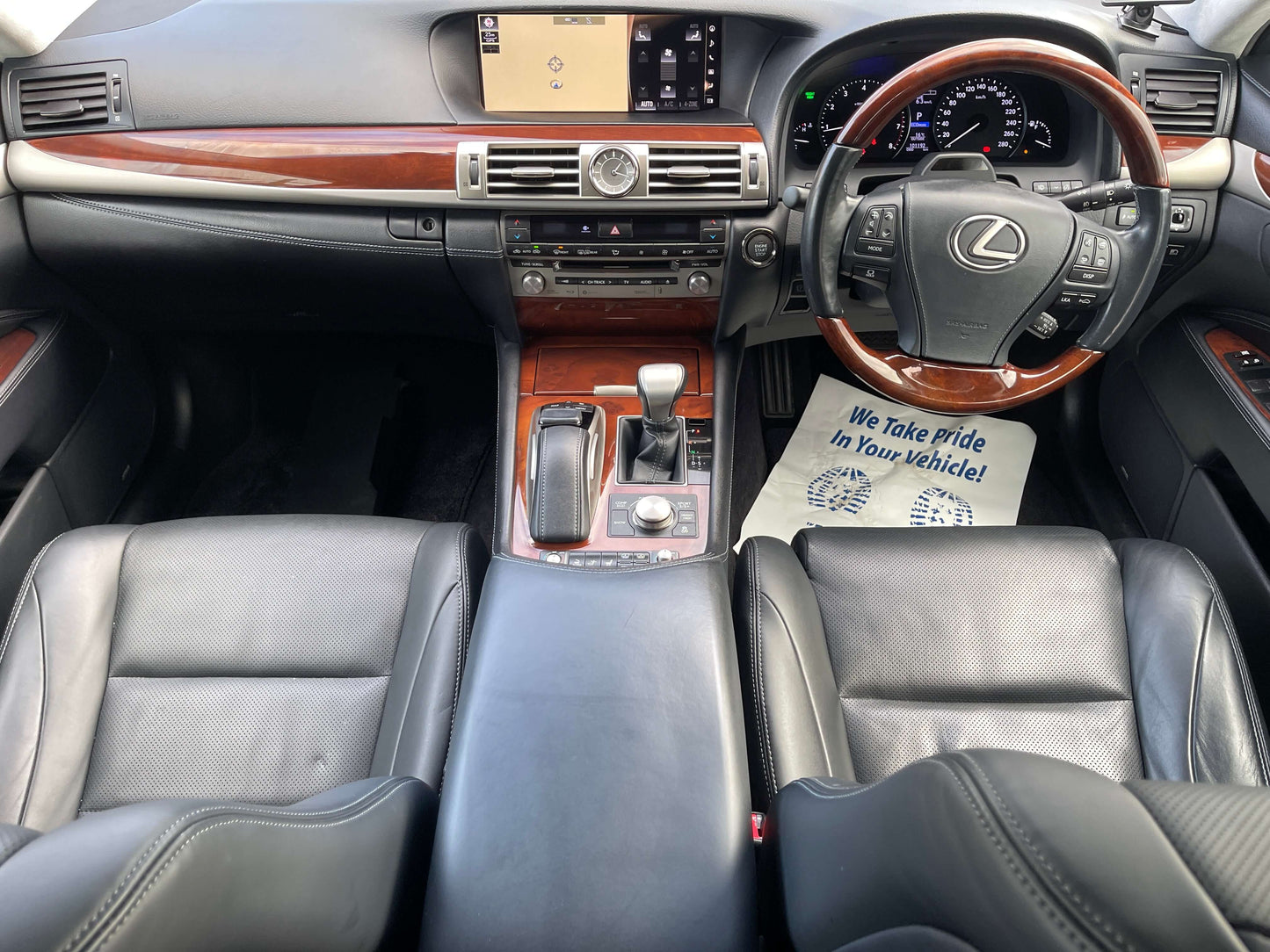 Interior view of a 2015 Lexus LS460 AWD V8 4.6L with black leather seats and wood trim, showcasing dashboard and center console.