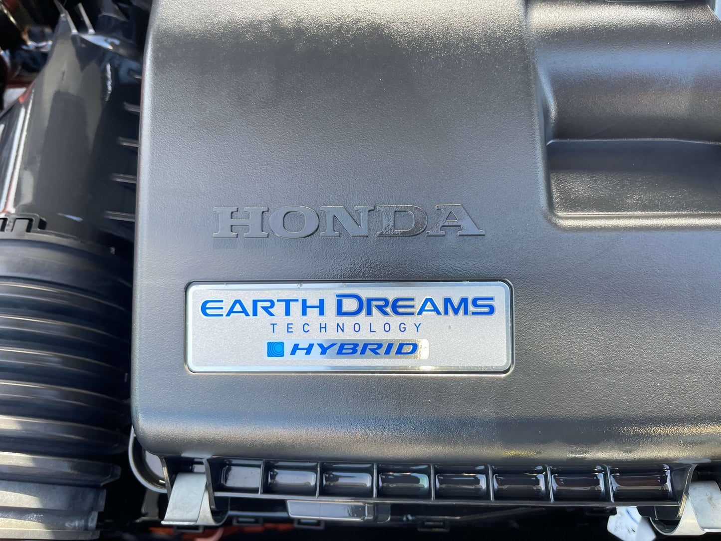 2020 Honda Fit 1.5 eHEV Close-up of the Honda engine cover showcasing Earth Dreams Technology and Hybrid badge.