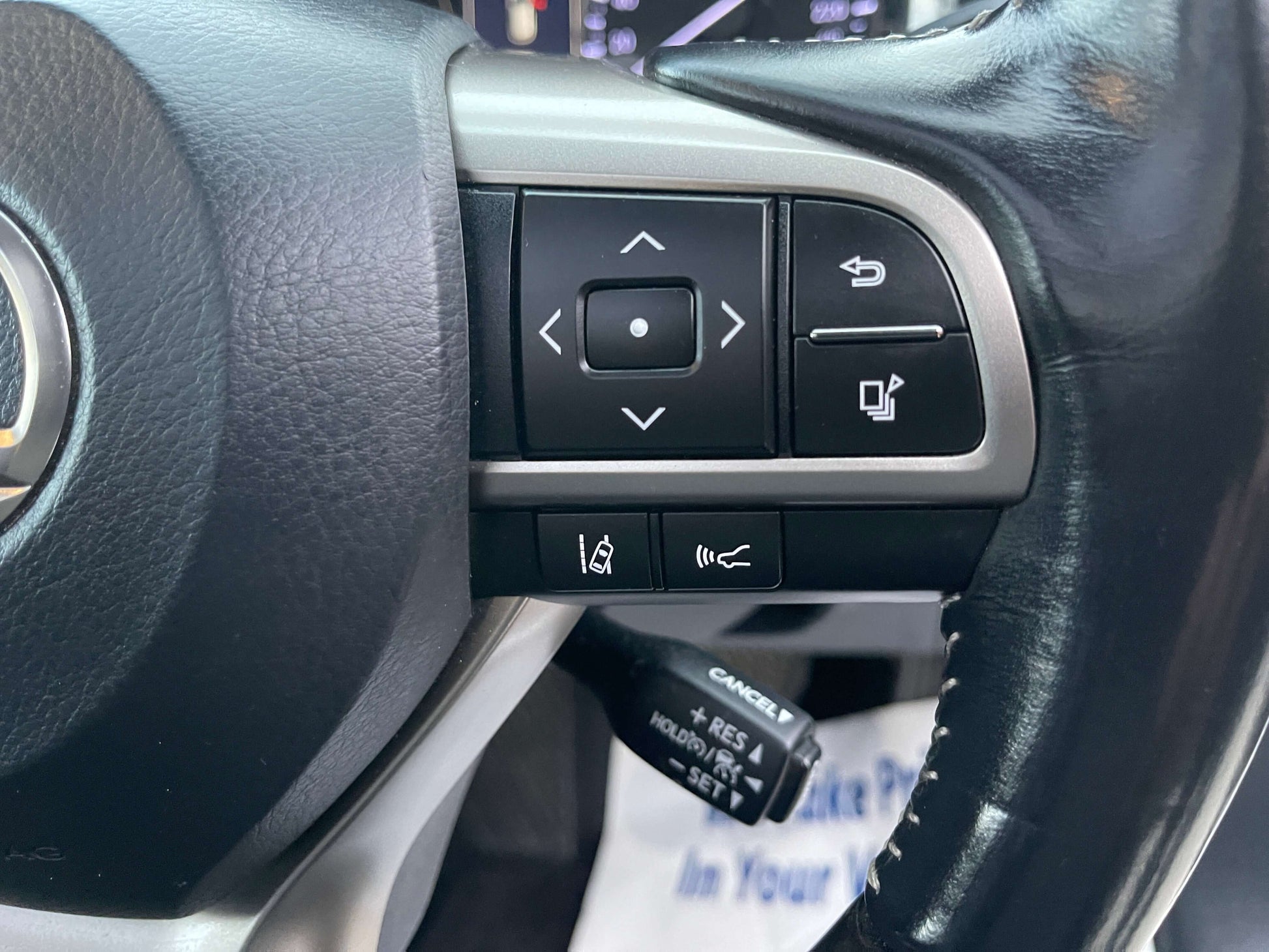 Close-up of the steering wheel controls of a 2017 Lexus RX450H hybrid SUV, featuring navigation and cruise control buttons.