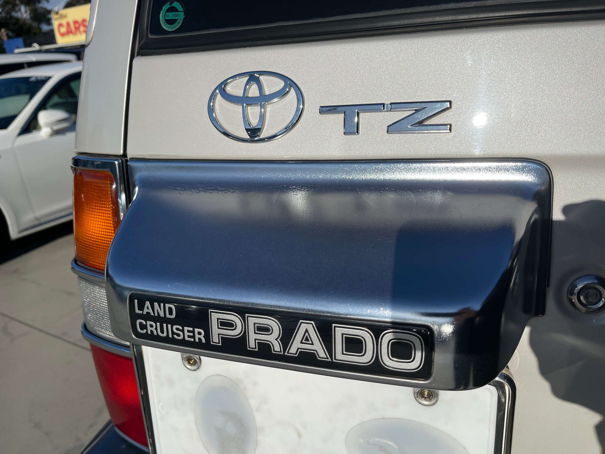 Rear badge of a 1996 Toyota Land Cruiser Prado V6 3.4L TZ showing the Land Cruiser and Prado logos.