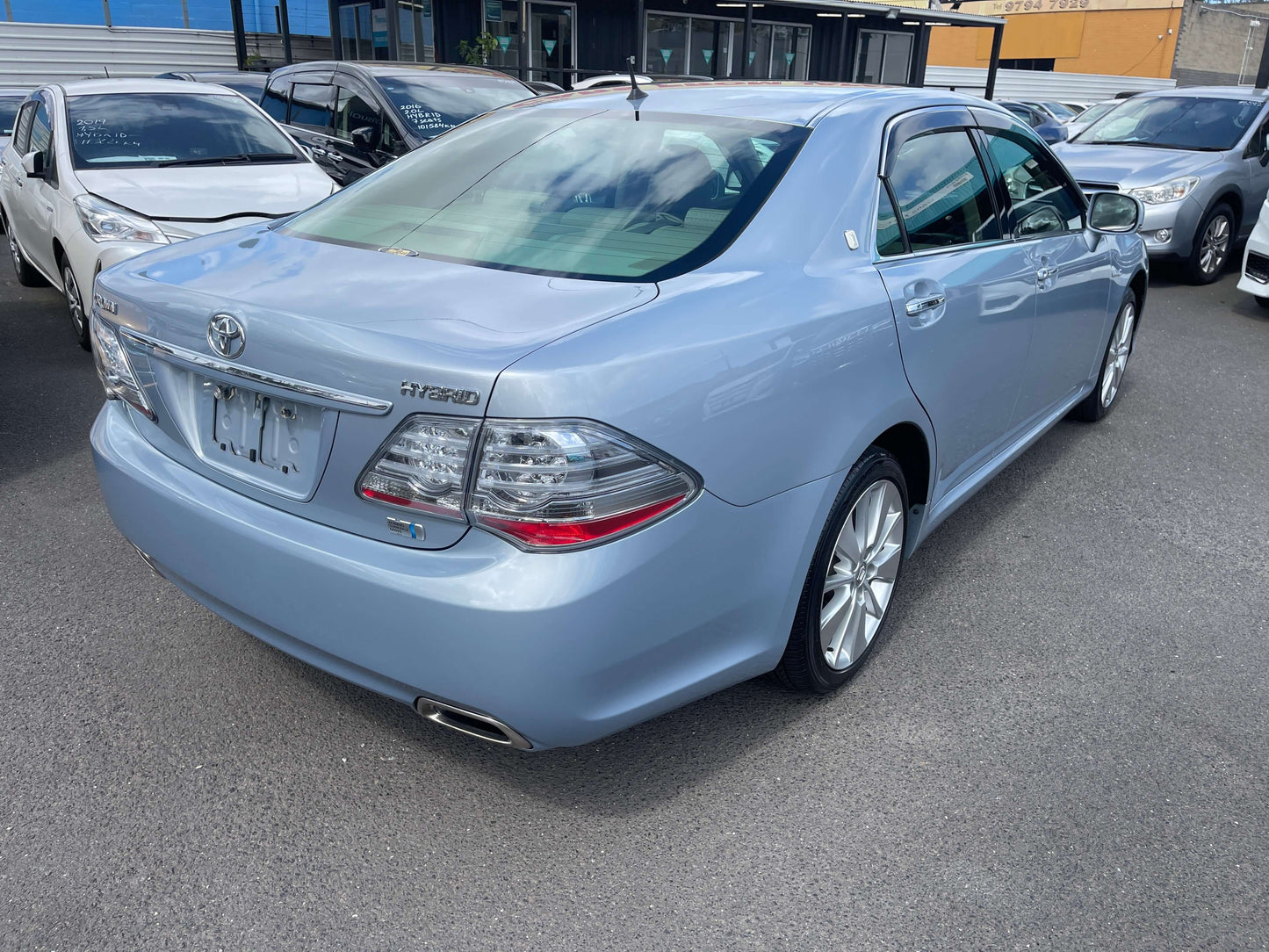2009 Toyota Crown V6 3.5L Hybrid luxury sedan in light blue color, parked among other vehicles.