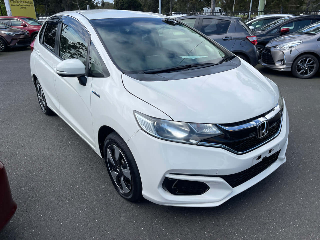 2017 Honda Fit 1.5L Hybrid white hatchback parked in a lot, showcasing its stylish design and compact size.