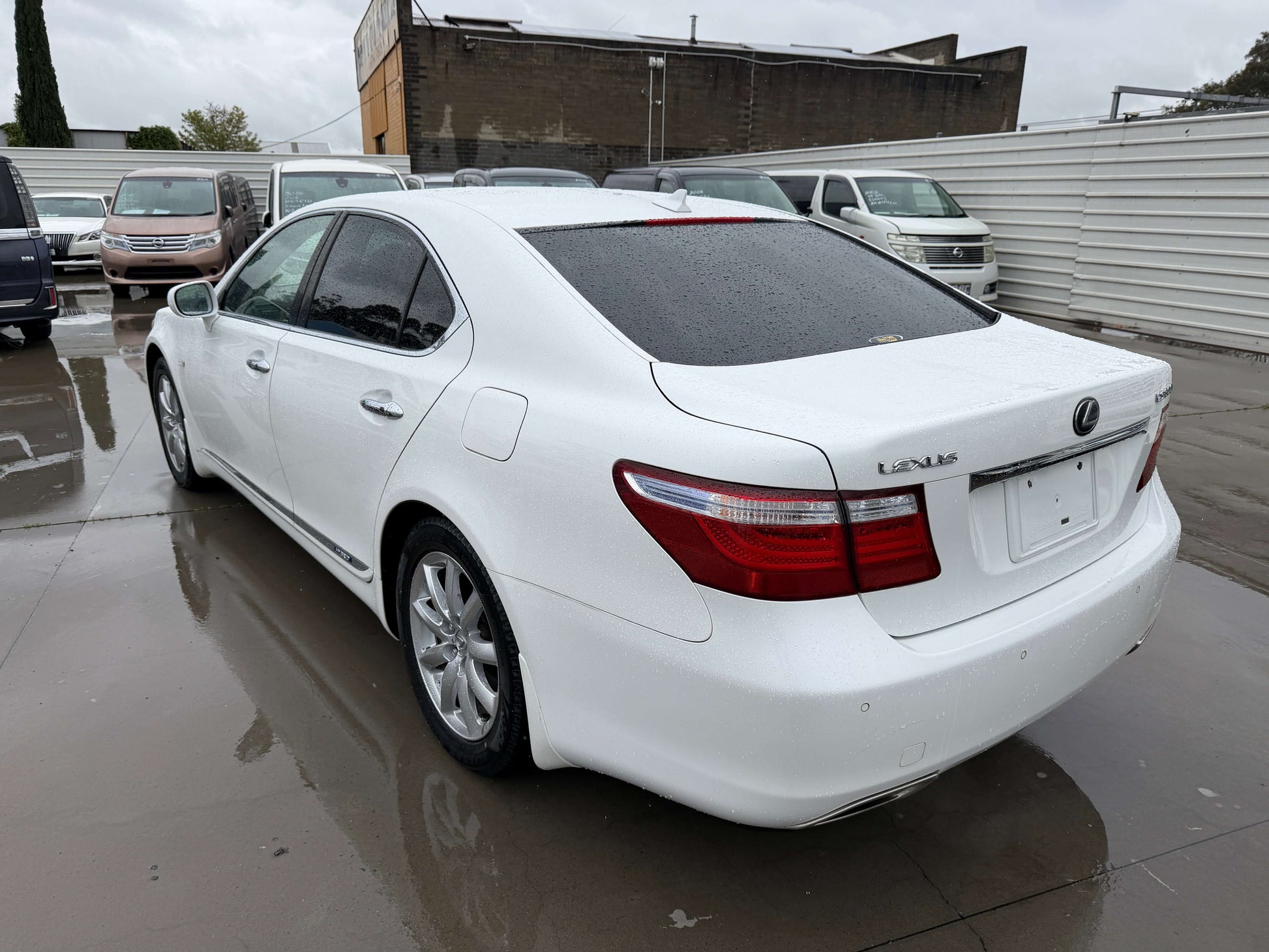 2007 Lexus LS600h AWD V8 5.0L Hybrid luxury sedan white exterior rear view, parked on wet pavement.