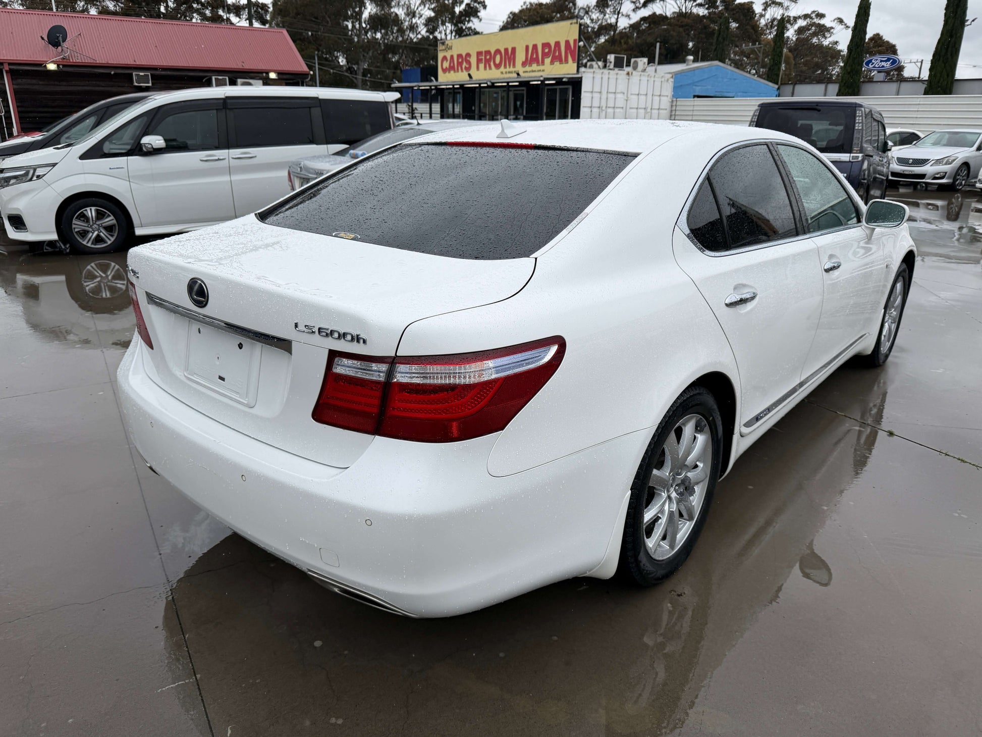 2007 Lexus LS600h AWD V8 5.0L Hybrid luxury sedan white rear view with wet ground.