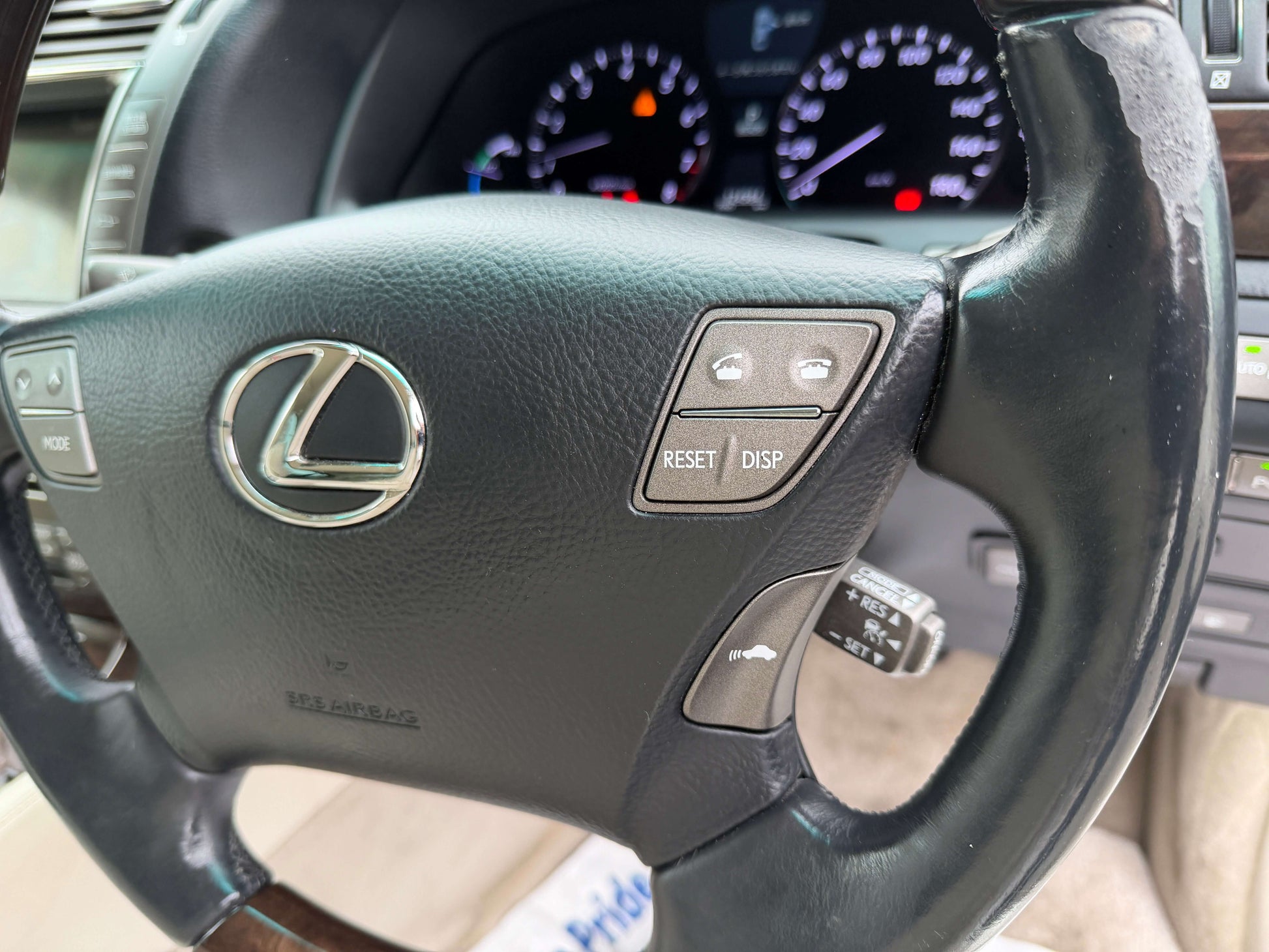 Steering wheel of a 2007 Lexus LS600h AWD V8 5.0L Hybrid with controls and dashboard dials visible.