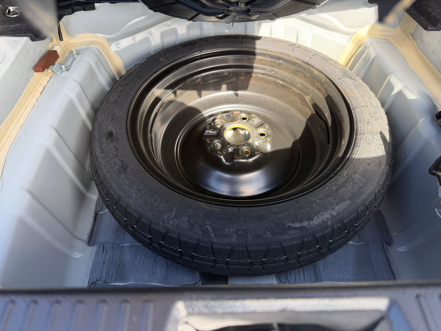2012 Toyota Crown V6 3.5L Hybrid Spare tire located in the trunk of a vehicle, showing black rim and tire tread.