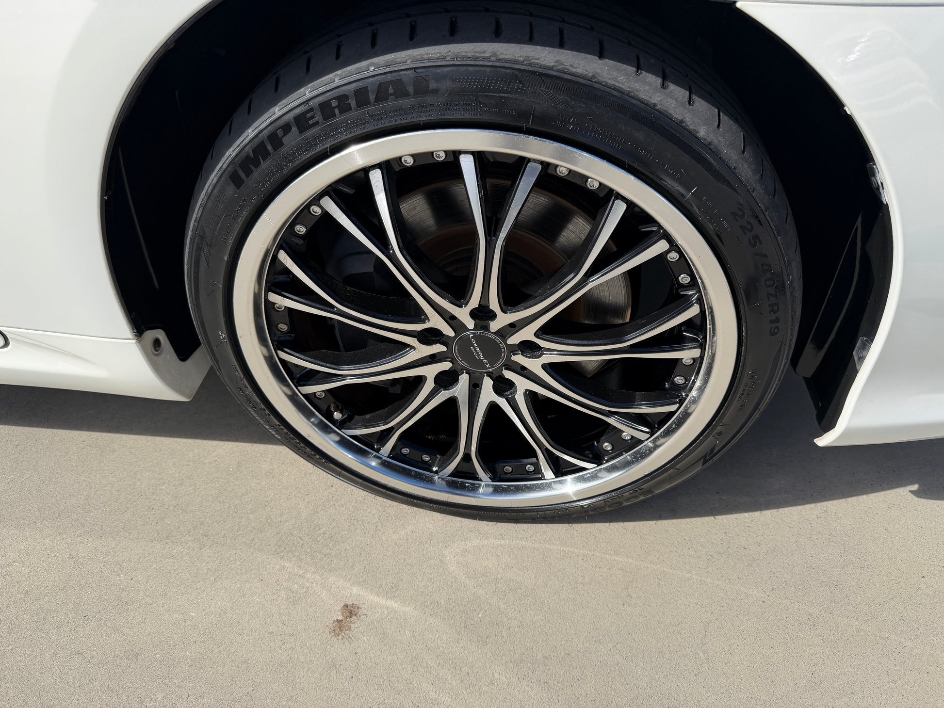 2012 Toyota Crown V6 3.5L Hybrid Close-up of a stylish black and chrome wheel on a white car, featuring an Imperial tire for enhanced performance.