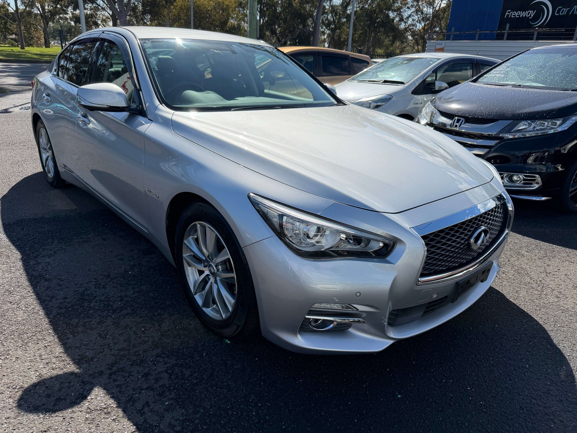 2014 Nissan Skyline V6 3.5L Hybrid sedan in silver parked, showcasing its sporty design and sleek lines.