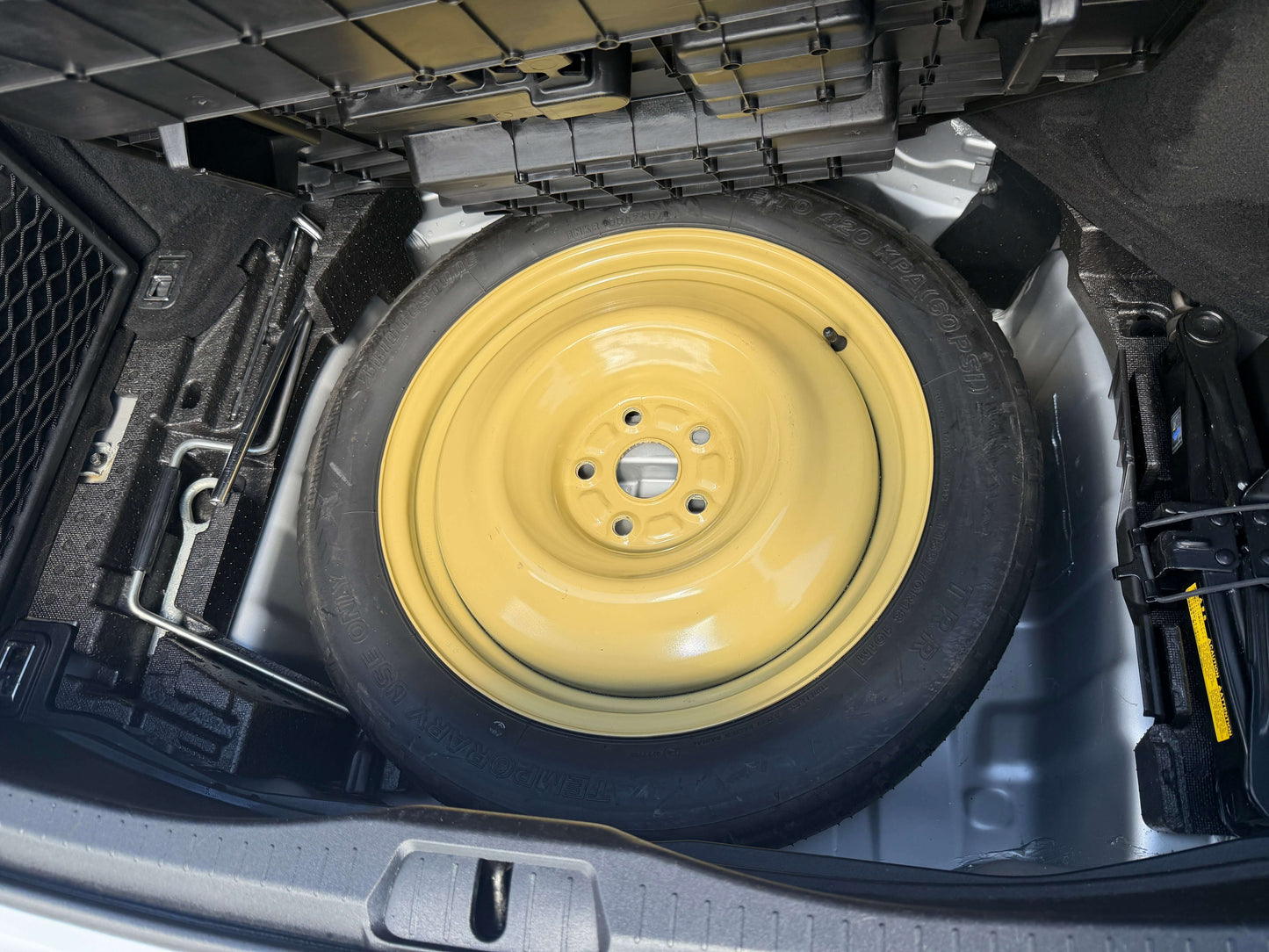 2007 Lexus LS600hL AWD V8 5.0L Hybrid Spare tire in trunk of a vehicle, featuring a yellow wheel and tools for roadside assistance.