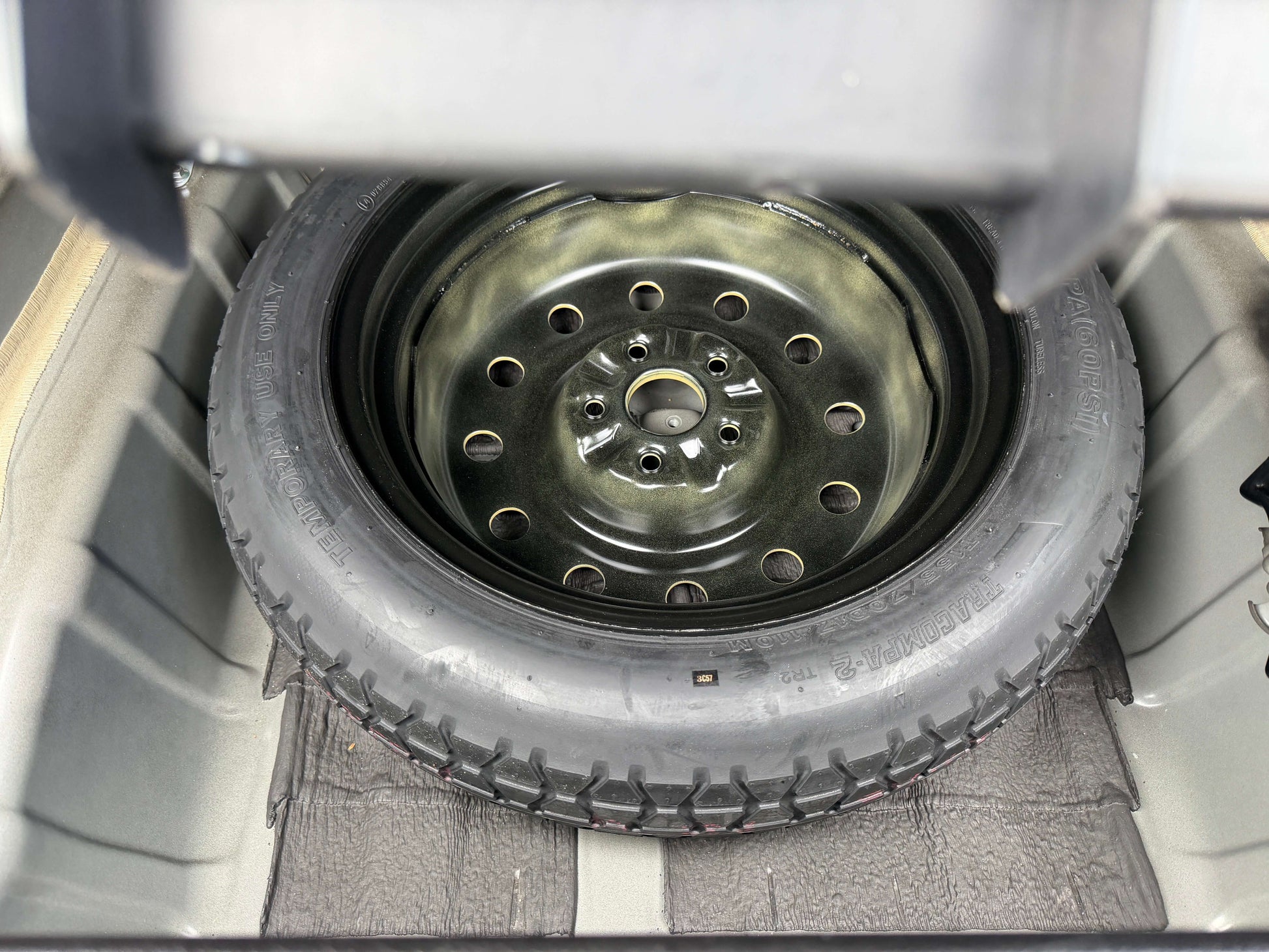 2008 Toyota Crown V6 3.0L Spare tire stored in the trunk of a vehicle, featuring a black wheel and tire, providing essential roadside assistance.