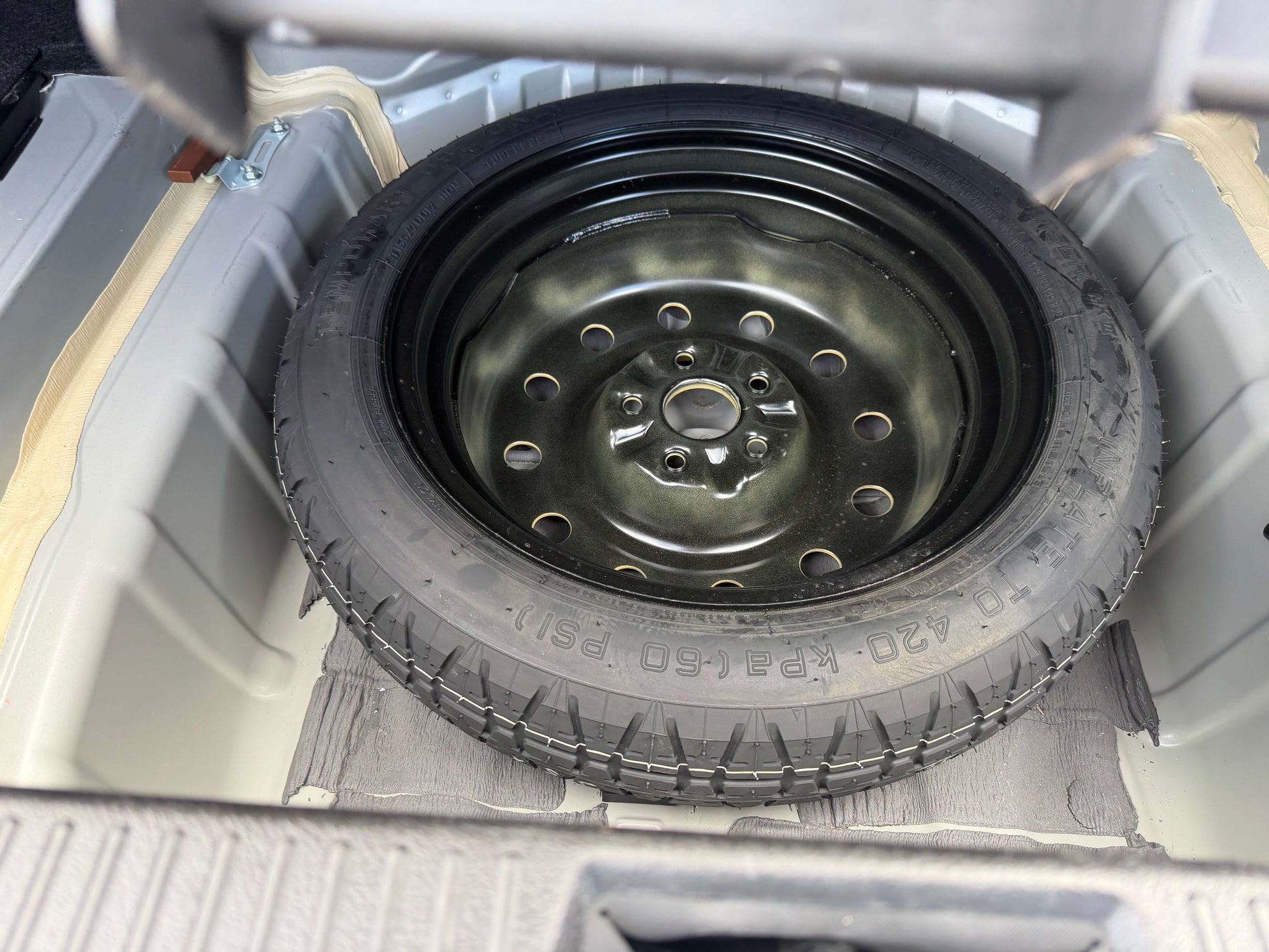 2010 Toyota Crown V6 3.0L Spare tire stored in trunk of a vehicle, showcasing a black rim and tread, ready for emergencies.