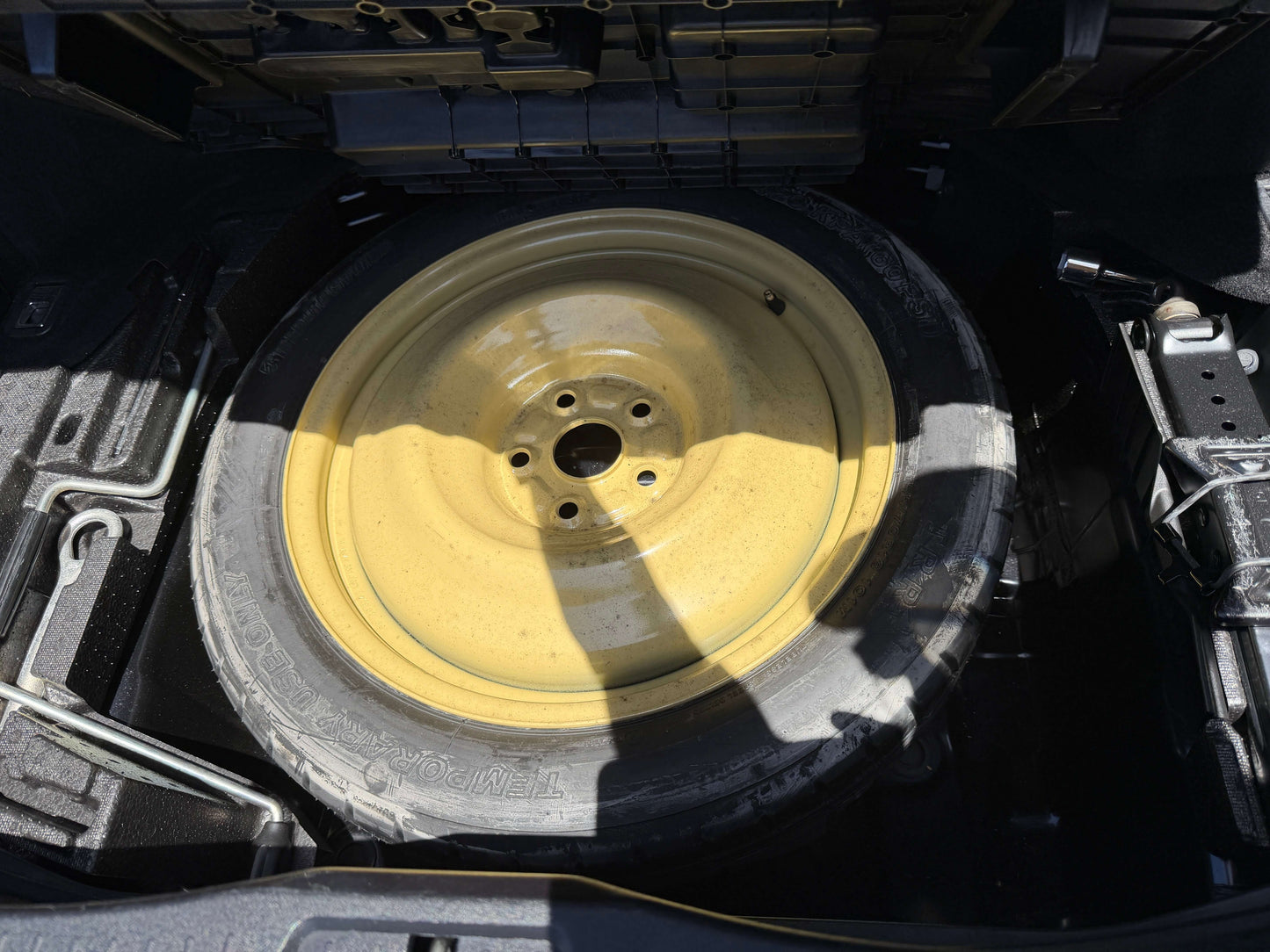 2007 Lexus LS600hL AWD V8 5.0L Hybrid Spare tire in the trunk of a car, showcasing yellow wheel rim and tire, designed for emergency use.