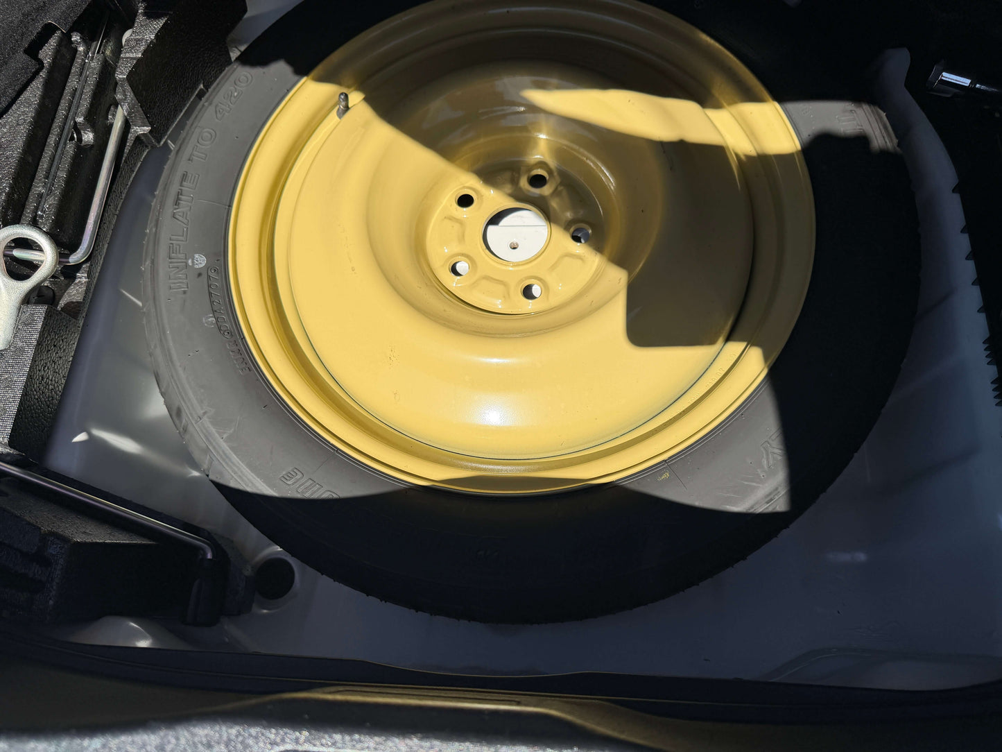 2007 Lexus LS600h AWD V8 5.0L Hybrid Spare tire with a yellow rim stored in the trunk of a vehicle.