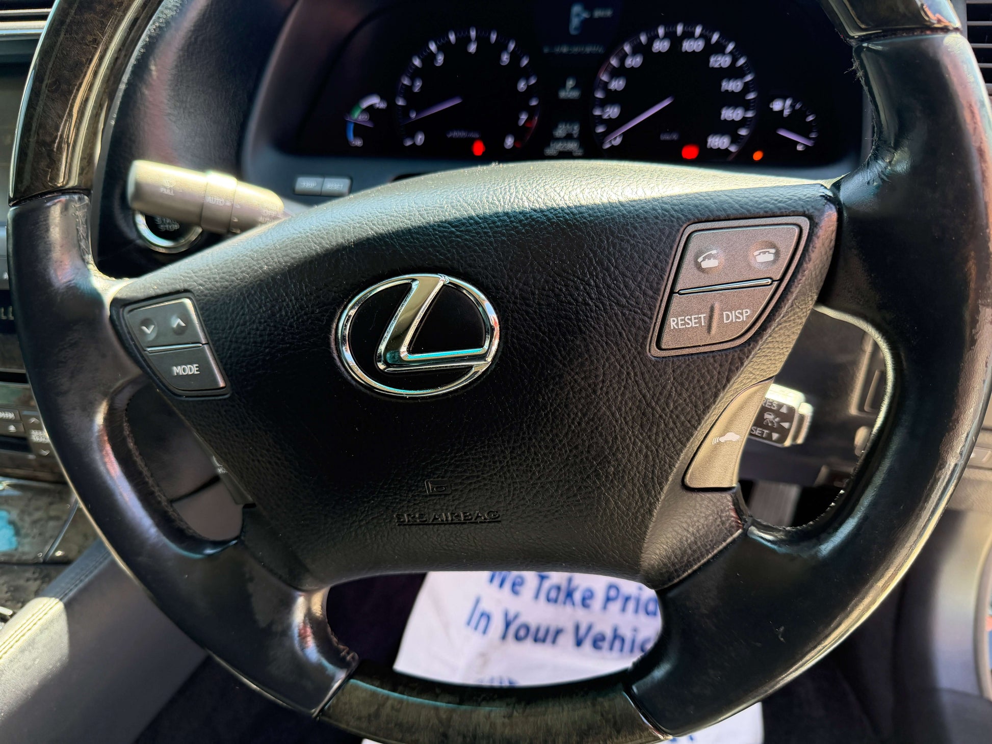 Close-up of the steering wheel of a 2007 Lexus LS600h AWD V8 5.0L Hybrid showing interior controls and Lexus logo.