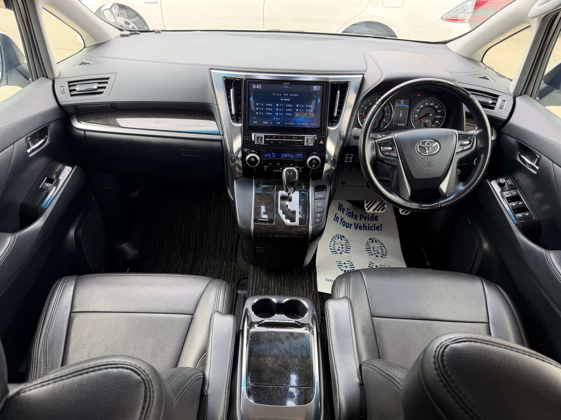 Interior view of a 2016 Toyota Alphard 2.5L showing dashboard, steering wheel, and black leather seats.