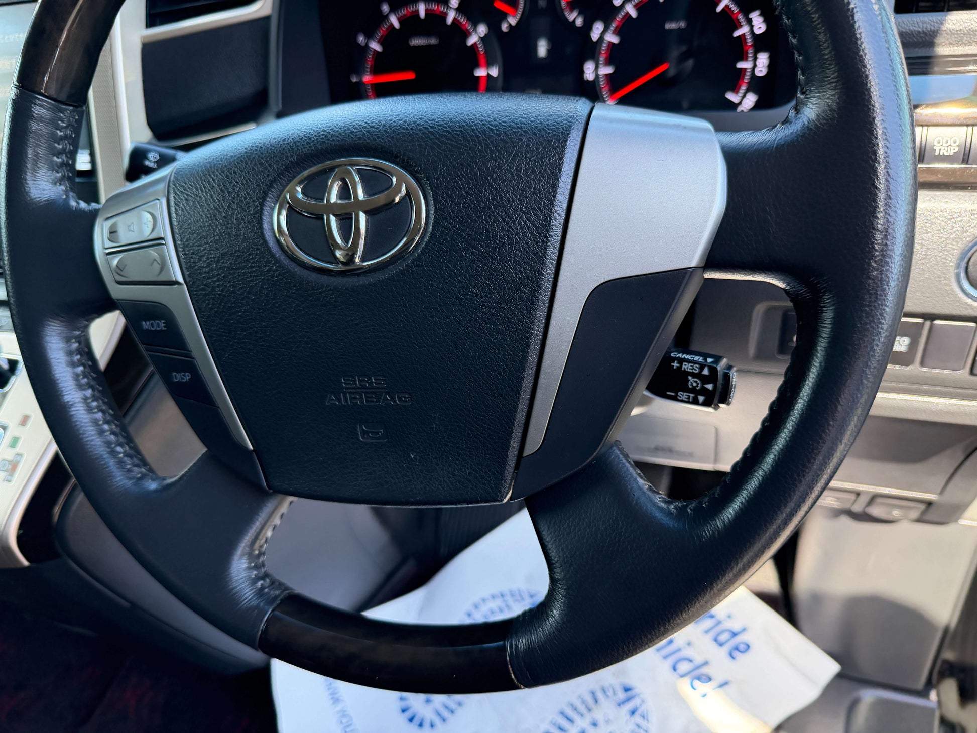 Close-up of the steering wheel of a 2013 Toyota Vellfire 2.4L Z Golden Eyes Edition, showcasing controls and the Toyota logo.