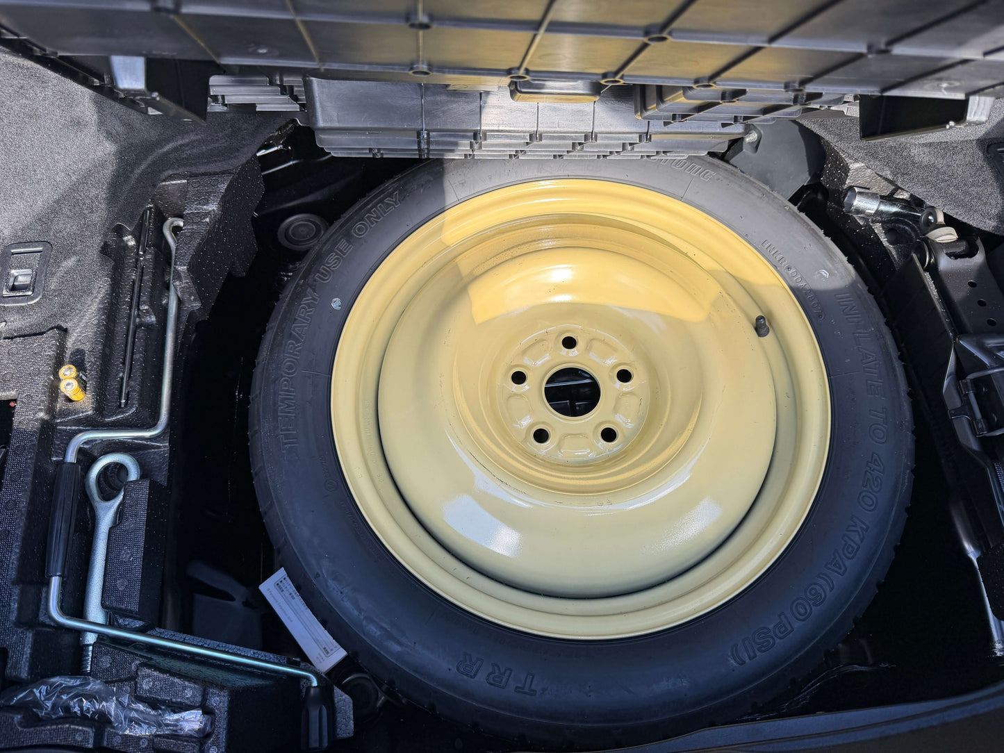 2007 Lexus LS600hL AWD V8 5.0L Hybrid Spare tire located in the trunk of a car, with a yellow wheel and black tire, ready for use.