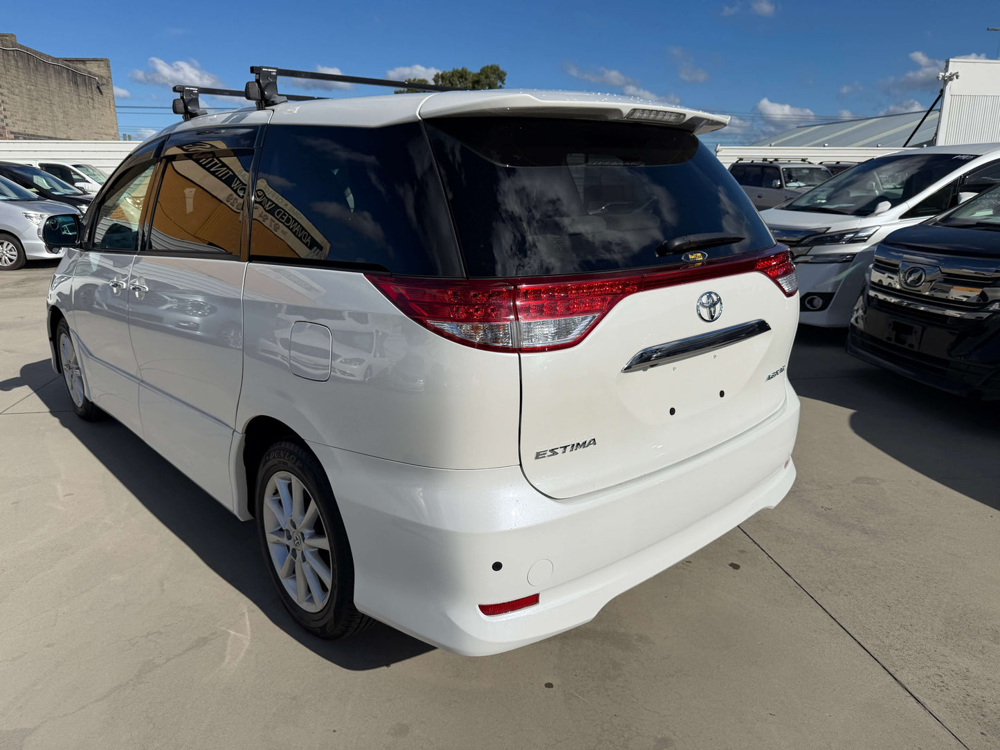 2010 Toyota Estima 2.4L 4WD Aeras G Edition white rear view with roof racks, showcasing the people's mover design.
