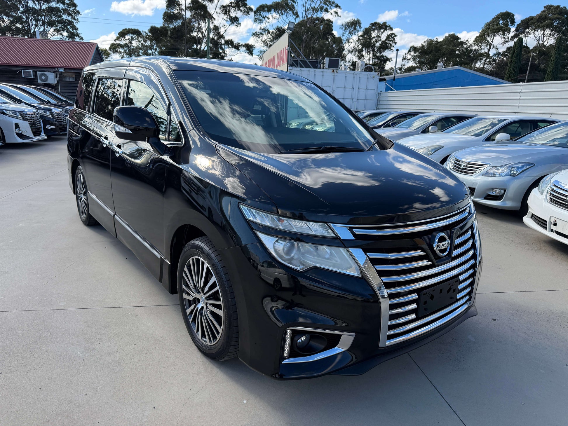 2015 Nissan Elgrand 2.5L 250 Highway Star parked with other vehicles in the background, showcasing its sleek design.