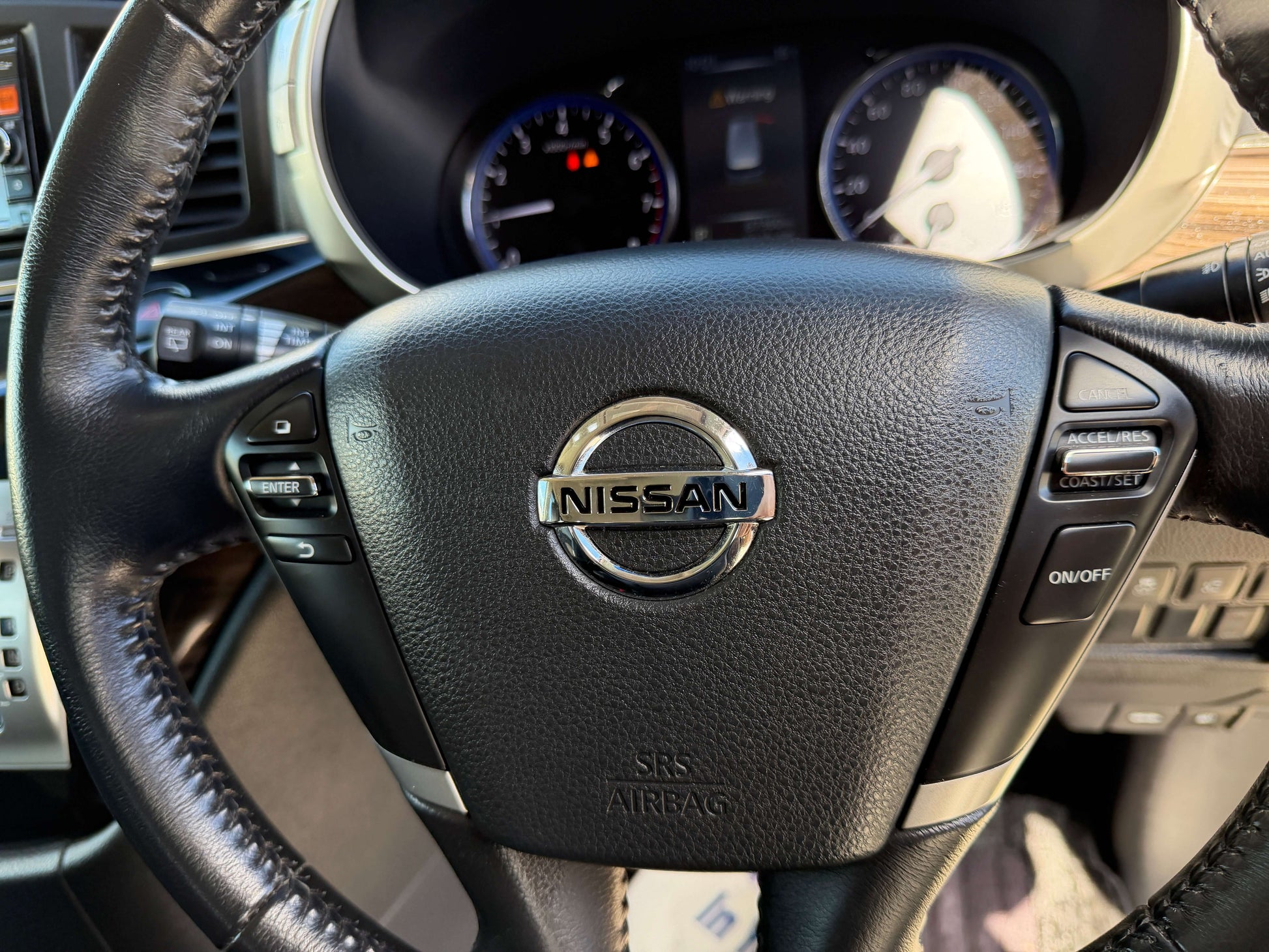 Close-up of the steering wheel of a 2015 Nissan Elgrand 2.5L featuring the Nissan logo and control buttons.