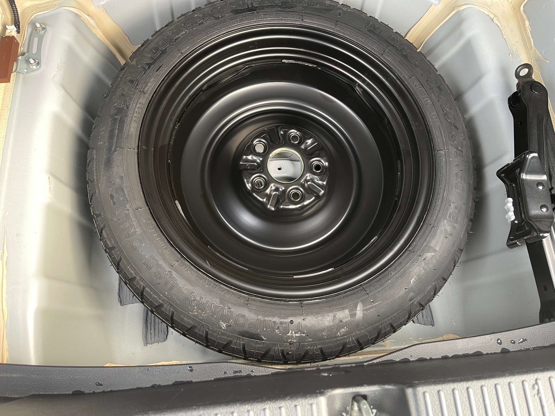 2011 Toyota Mark X Spare tire of a vehicle in the trunk, featuring a black rim and tread, ready for emergencies.