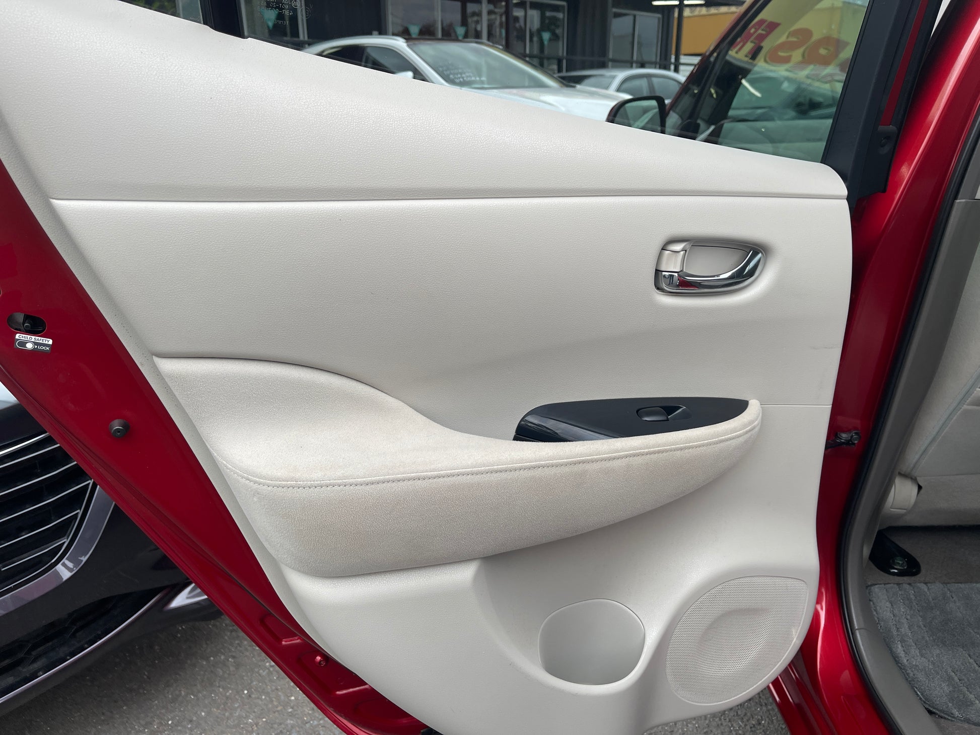 Interior door panel view of a 2013 Nissan Leaf 24kW G-Edition Full Electric showcasing beige fabric and controls.